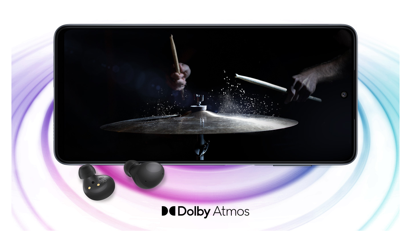 Galaxy M33 5G in landscape mode and an image with a person playing drums in the black background onscreen. A pair of black Galaxy Buds2 are placed in front of the device. On the right bottom is a logo for Dolby Atmos.