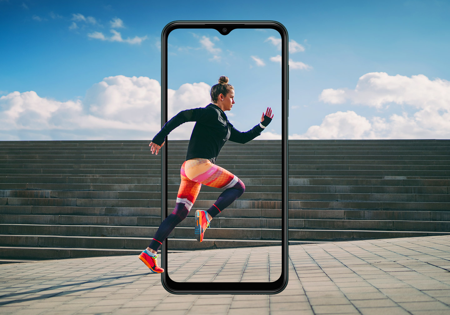 The outline of a Galaxy M13 FHD+ 6.6-inch infinity V Display is set in portrait mode in front of a wide set of concrete stairs. Above the stairs is a blue sky with clouds. Onscreen is a woman running in full stride, with her hands and feet extending beyond the frame of the display.