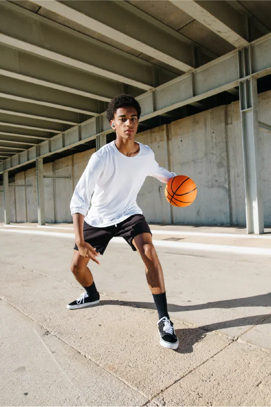 A boy wearing JBL true wireless earbuds while playing a basket ball.