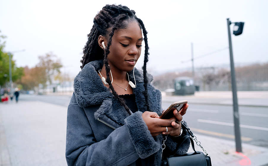 Girl wearing JBL Tune 235BT wireless earbuds while checking her phone and enjoying music in a relaxed lifestyle setting.