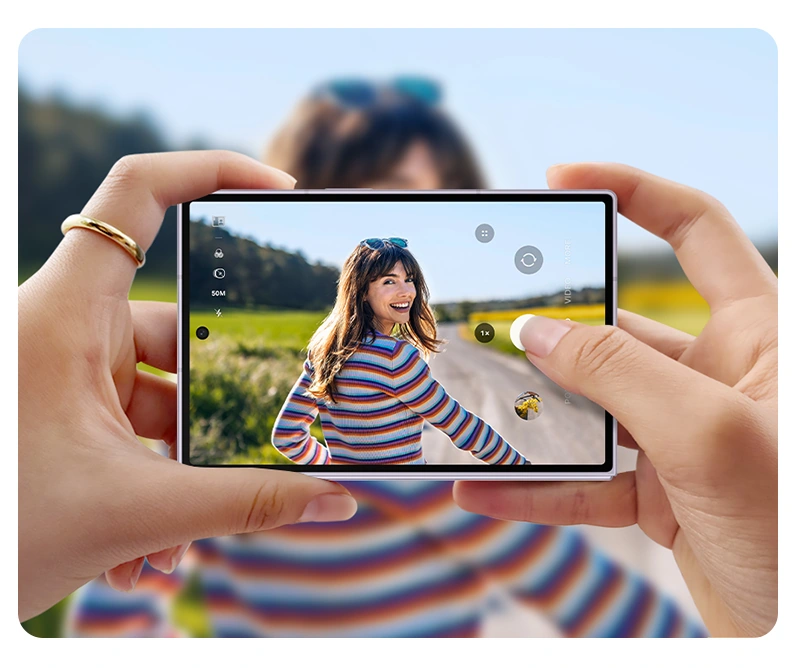 Photo of someone is being taken in front of a scenic background on Galaxy Z Fold8. The device is folded and being held horizontally. The photo can be seen on the cover screen.