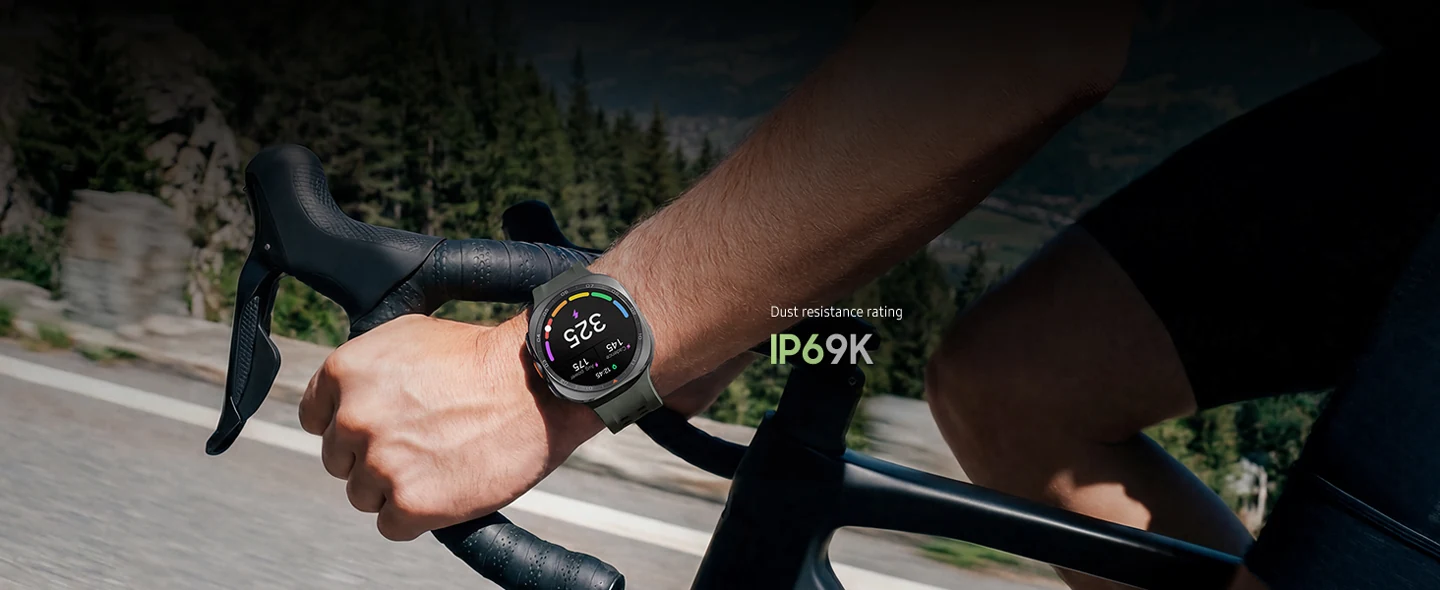 A cyclist is riding a bike on a road in the mountains while wearing a Galaxy Watch Ultra2 in Titanium Silver with a Marine Band in Olive displaying a personalized Functional Threshold Power with cadence and average power.