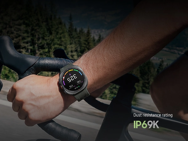 A cyclist is riding a bike on a road in the mountains while wearing a Galaxy Watch Ultra2 in Titanium Silver with a Marine Band in Olive displaying a personalized Functional Threshold Power with cadence and average power.