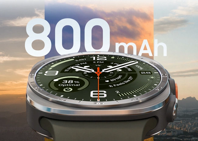Galaxy Watch Ultra2 in Titanium Silver with a Marine Band in Olive, shown up close facing front and angled upward. The background shows three different skyline and cityscape views at different times of day to demonstrate the large 800 mAh battery capacity.